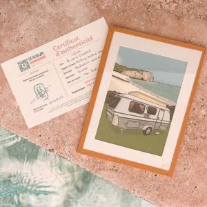 Illustration encadrée d’une caravane devant une falaise en bord de mer, posée avec son certificat d’authenticité.