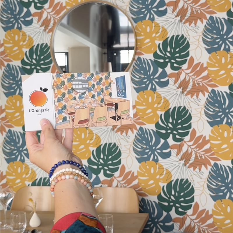 Bon cadeau de l'Orangerie posé devant le papier peint de la salle, motifs en harmonie