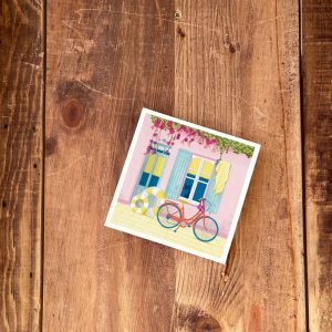 Illustration d'une façade de maison rose aux volets bleu lagon, avec un vélo rouge, une bouée gonflable jaune et blanc, une bougainvillée et un chat à la fenêtre.